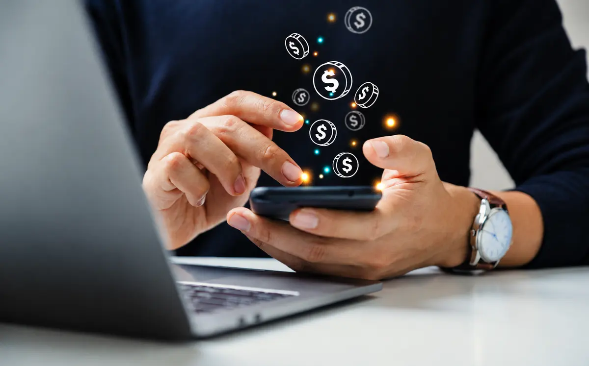Empresário usando o celular, com ícones de moedas de dólar saindo da tela